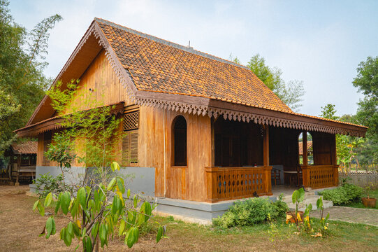 Traditional Betawi Tengah house with a tiled roof, wooden facade, front veranda, decorative details, and surrounding greenery in Jakarta, Indonesia.