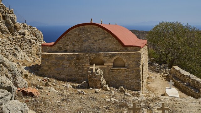 Small stone church with red roof in a barren landscape surrounded by crosses, Lost Place, Abandoned Village, Mikro Chorio, Church of the Assumption of Mary, Zero Waste Island, Tilos, Dodecanese, Greek Islands, Greece