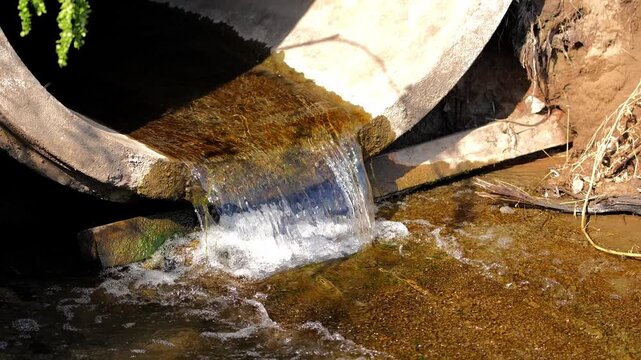 Close-up shot of clear water rushing out of a massive industrial concrete drainage pipe into a natural stream bed.