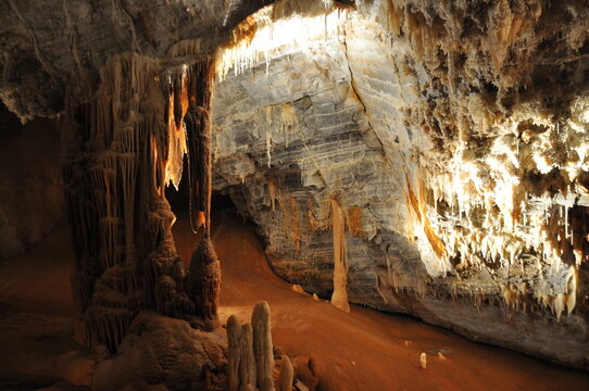 Stalactites, a stalagmite column, layered rock and hanging aragonite crystals lit inside the Gouffre G&eacute;ant de Cabrespine, Aude, France.