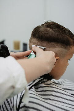 A female hairdresser cuts the back of a little boy's head with a clipper. A professional hairdresser and a child client in a modern barbershop.