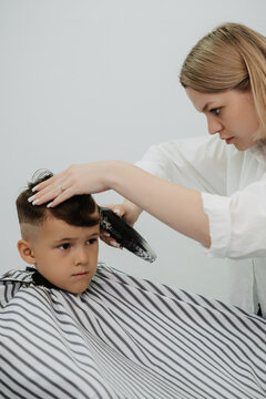 A female hairdresser cuts the back of a little boy's head with a clipper. A professional hairdresser and a child client in a modern barbershop.
