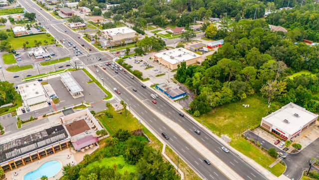 Aerial view of a busy intersection with suburban retail businesses and surrounding green trees busy road suburban landscape retail stores traffic flow road network daylight
