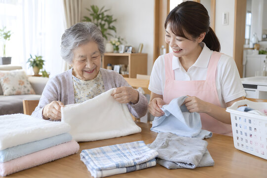 Elderly Japanese woman folding laundry with a female caregiver at home