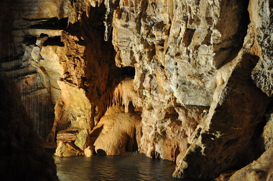 Flowstone cascade and stalactites above a dark underground pool with dripping water inside the Gouffre G&eacute;ant de Cabrespine, Aude, France.
