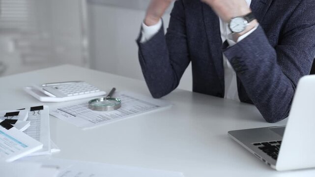 Businessman analyzing financial documents and preparing reports, performing audit work in the office with a stack of paperwork, calculator, magnifying glass, and laptop. Audit and taxes