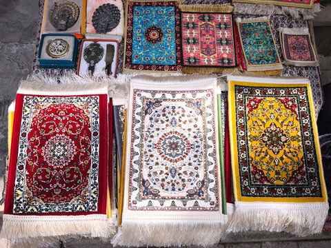 Traditional small Azerbaijani carpets, mouse pads, and authentic vintage souvenirs displayed at an outdoor street souvenir shop in Old City Baku. High angle view of miniature silk and woven rugs 