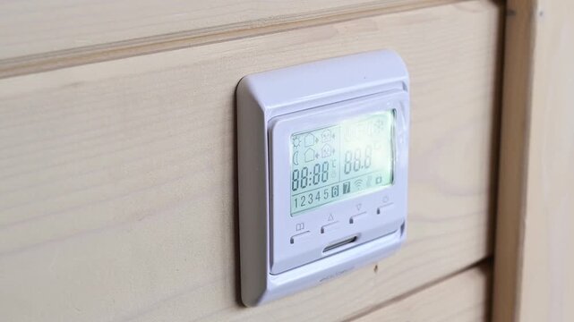 Woman adjusts wall-mounted digital thermostat by pressing control button to regulate indoor temperature and maintain comfortable home climate