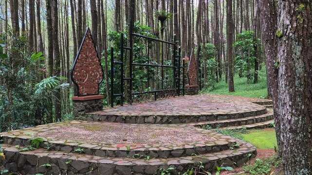 Scenic open air stone performance stage decorated with traditional Javanese wayang gunungan, located in the middle of a dense green pine forest park in Indonesia for outdoor events and ecotourism