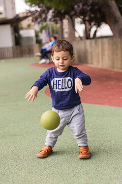 Young toddler playing with ball on playground surface