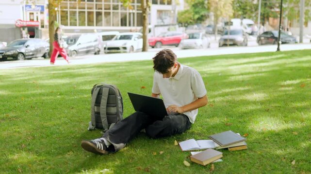 Dedicated young guy looking away before typing on a laptop in the park.