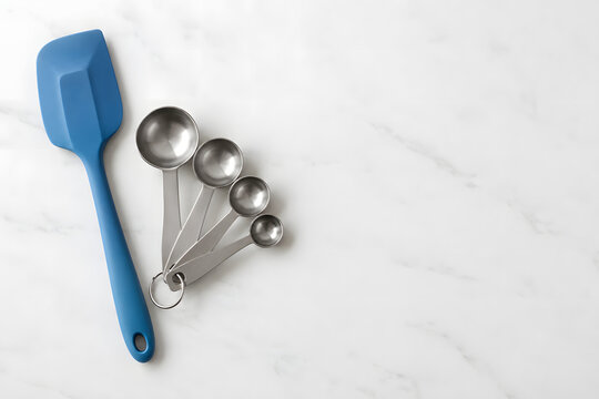 Blue silicone spatula and metal measuring spoons on a white baking surface