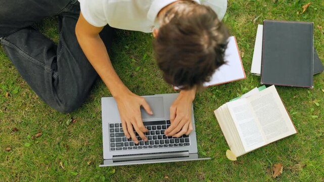 Top down view of human hands typing on a laptop during an outdoor study session.