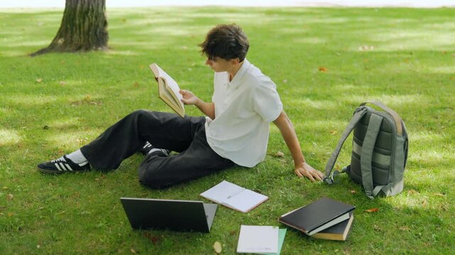 Dedicated caucasian scholar learning from a textbook in the outdoor park.