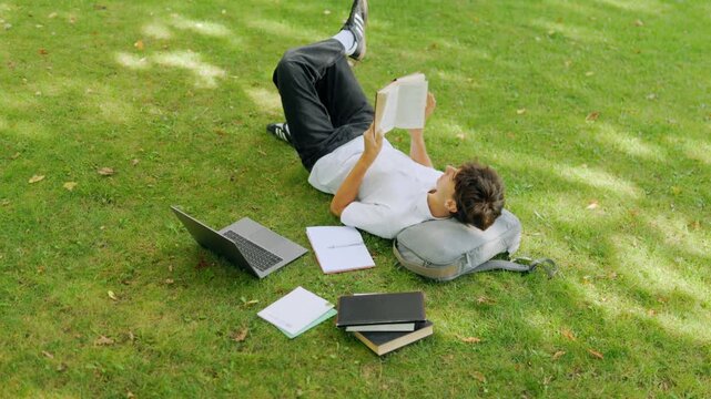 Top down view of a young teenager reading a book on the outdoor grass.