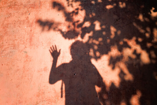 Shadow of leaves texture with male hand waving gesture on the red dirty wall