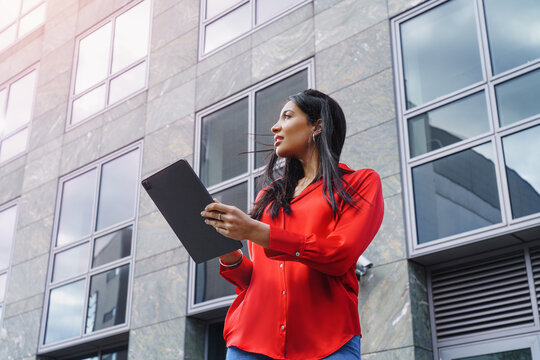 Successful businesswoman standing outside a corporate office building with a digital tablet. Outdoor portrait of a woman. Success, work motivation, and career vision. Copy space.