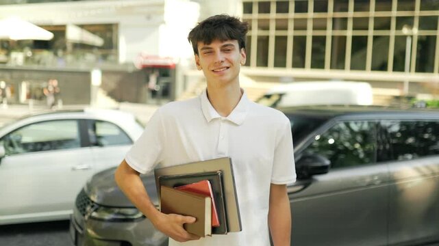 Smiling teenage student holding study books standing on the urban street.