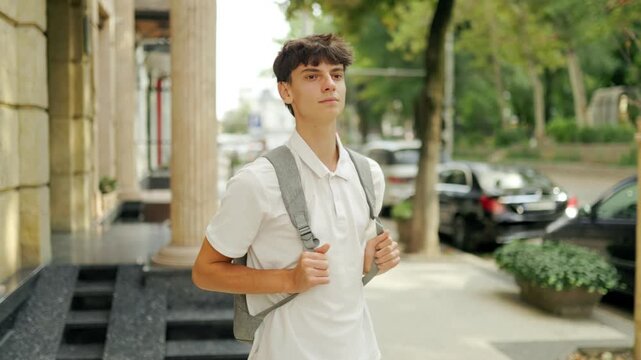 Dedicated caucasian learner wearing a backpack standing near the college entrance.
