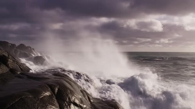 Ocean waves crashing against rugged coastal rocks, creating white foam and water spray. Dramatic natural seascape with powerful waves and rocky shoreline.