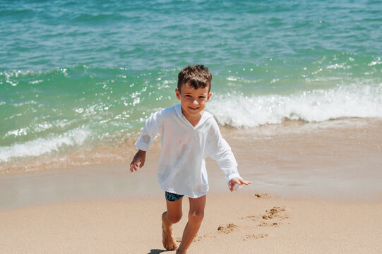 Happy kid playing on the beach in rough waters during a summer vacation
