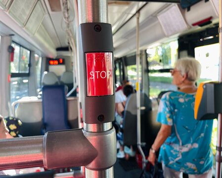 Inside a public bus, theres a stop request button and various passengers. One person is standing while another person is seated comfortably