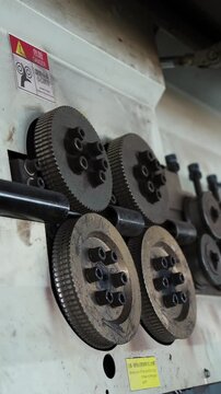 Grooved drive rollers pushing a steel bar through a rebar bending machine at a factory
