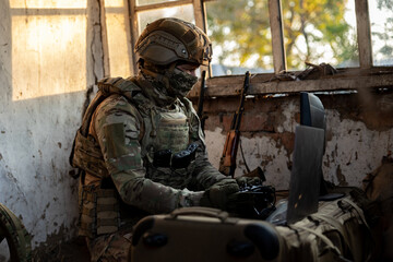 Obraz premium Soldier operates a drone control console. Military personnel is carrying out a combat mission at a position in an abandoned house.
