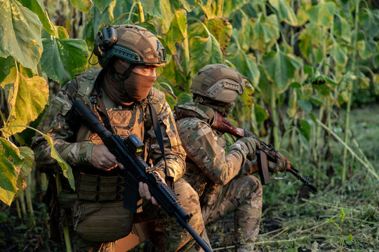 Military Soldiers with assault rifles at a combat position in a field. Military personnel carrying out a combat mission.
