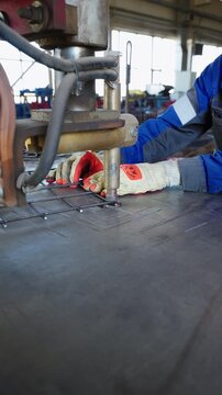 Worker in gloves holding a steel mesh under a spot welding machine at a factory
