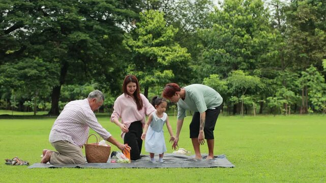 unfold picnic mat in green city park. Happy Asian family having fun time on picnic