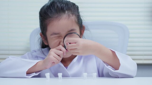 Little girl scientist examining fake teeth model with magnifying glass during dental study session at desk