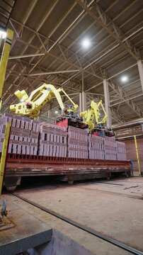 Robotic arms stacking red bricks onto a kiln car at a brick factory