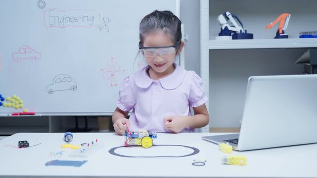 Little girl student programming small robot and celebrating success during stem education class in classroom