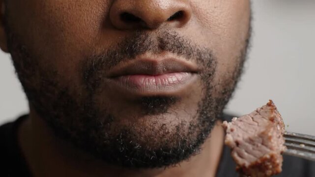Bearded man eating grilled beef steak piece with a metal fork