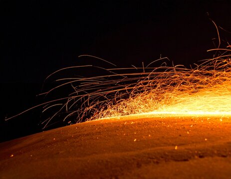 Glowing amber embers and flying sparks on a dark background, warm abstract with copy space