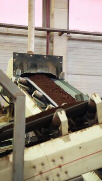 Red clay moving on a conveyor belt under a metal hood at a brick factory