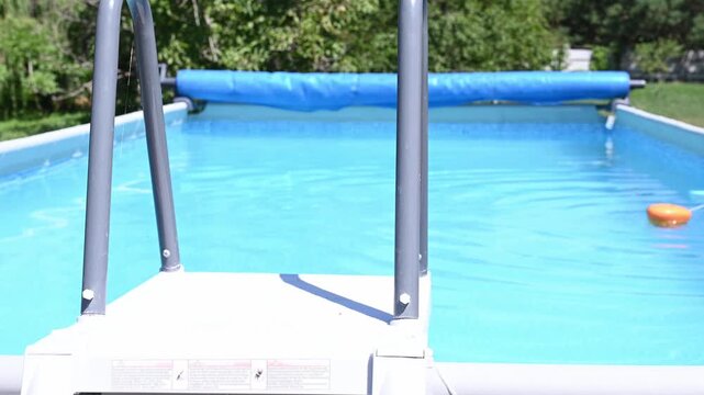View from pool access steps over clear water inside frame swimming pool, highlighting summer recreation, outdoor leisure, backyard relaxation and private swimming.