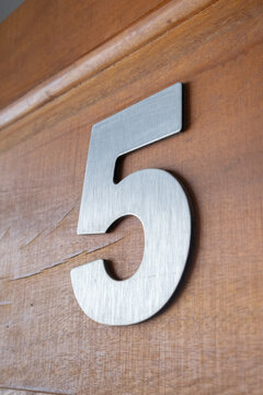 Vertical extreme close-up angle of a modern brushed metal number five fixed to a warm wooden surface