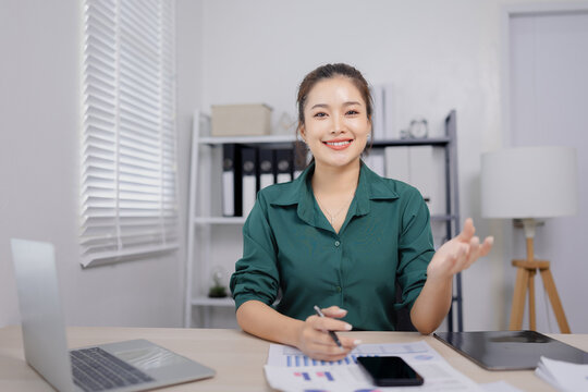 Asian businesswoman working at her desk, reviewing financial reports and documents in a modern office environment.