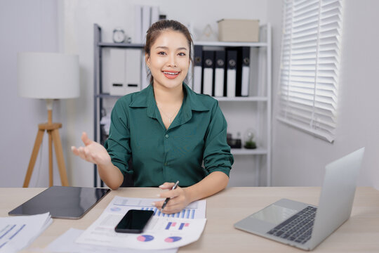 Asian businesswoman working at her desk, reviewing financial reports and documents in a modern office environment.