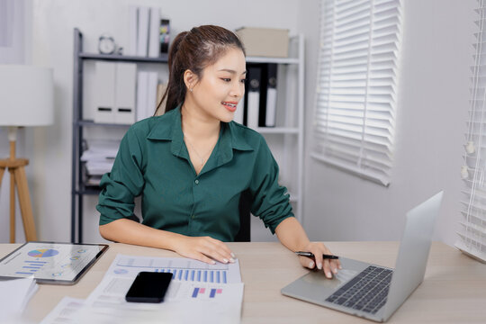 Asian businesswoman working at her desk, reviewing financial reports and documents in a modern office environment.