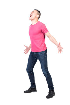 Full body of young annoyed man with dark hair in casual clothes screaming loudly with closed eyes and outstretched arms