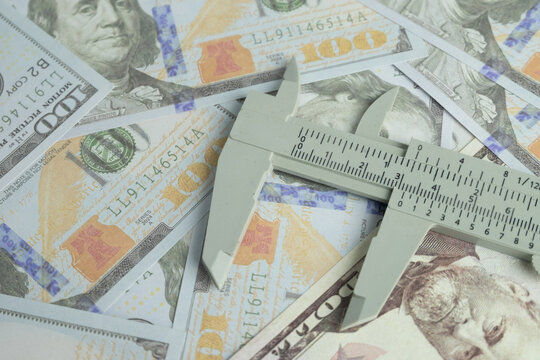 Vernier caliper resting on scattered US dollar bills. Concept of measuring wealth, financial precision, budget control, cost estimation, inflation rate, and business economic profit analysis.