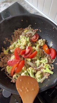 Stir fry vegetables meat cauliflower tomato pan home cooking person healthy fresh meal preparation joyful kitchen dinner wok pork wooden spatula culinary skills delicious warm domestic energy