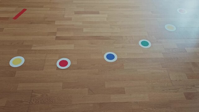 Multicolored circular signs on a wooden parquet floor indicating a path for children's motor games or for social distancing rules