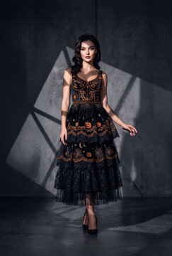Beautiful woman in elegant Halloween dress with pumpkin and spiderweb embroidery