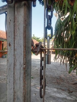 Old padlock and metal chain securing the entrance gate of a building in a rural area of Java, Indonesia, representing security, protection, access control, and restricted entry.