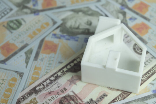 Close up of a white miniature house model resting on scattered US dollar bills. Concept of real estate investment, property mortgage, housing loan, property tax and saving money for a new home.