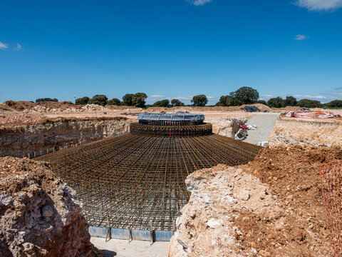 A comprehensive wide shot of a deep excavation showcasing the full scale of steel rebar reinforcement for a wind turbine foundation under a clear sky.